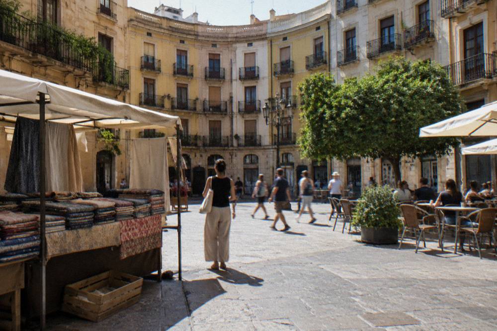 A narrow Valencia street with market stalls and cafe tables set out under old stone buildings