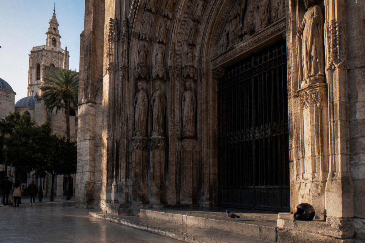 Gothic cathedral doorway in Valencia with stone carvings and a barred entrance under morning light
