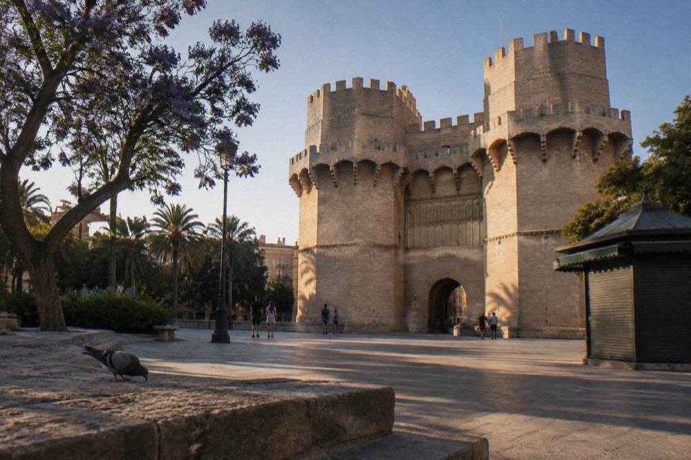 Gothic stone gate tower of a medieval city wall seen from a sunny square below