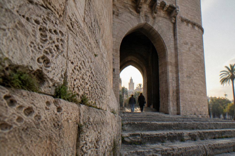 A Gothic stone gateway in Valencia with arched openings and people-sized doorways set into the ancient wall.