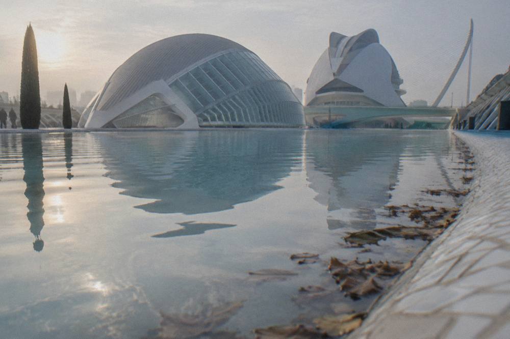Long reflecting pool stretching between white futuristic buildings under an open sky