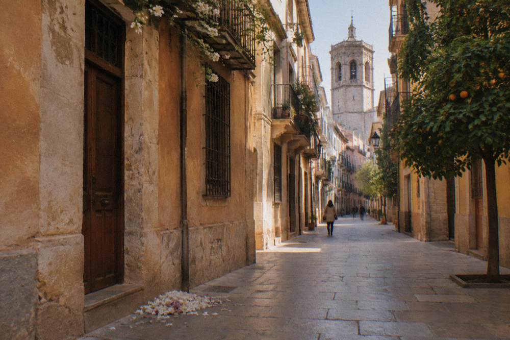 A pedestrian street in Valencia old town with pastel facades and a church tower in the distance