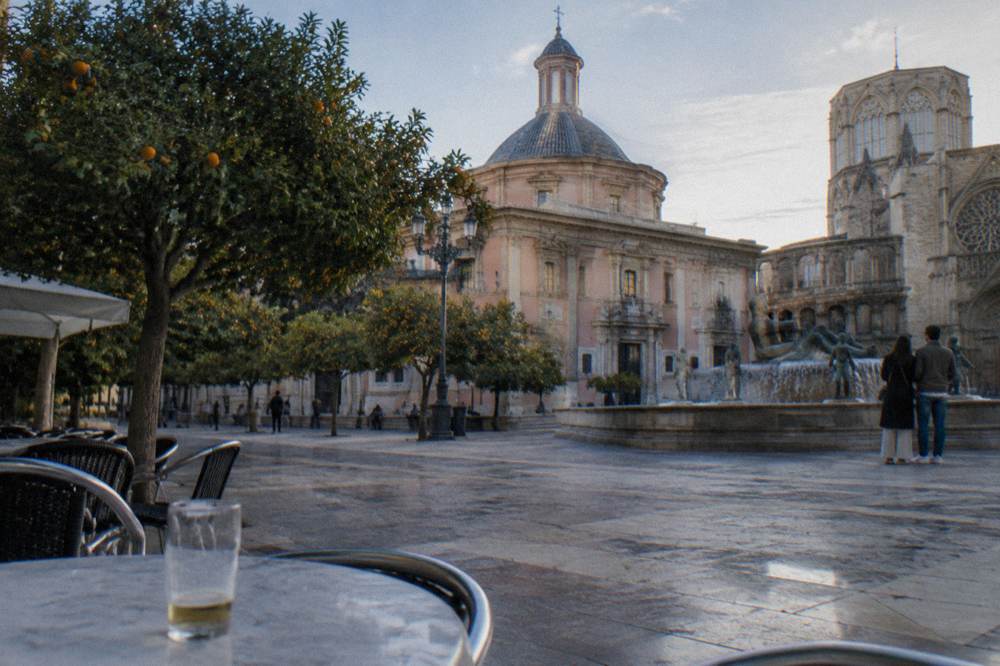 Small square with a church facade and cafe tables under trees