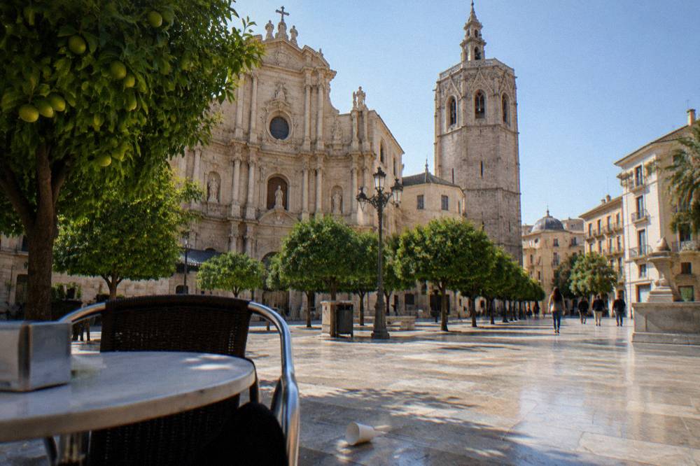 Sunlit square with the Valencia cathedral facade and its bell tower above orange trees