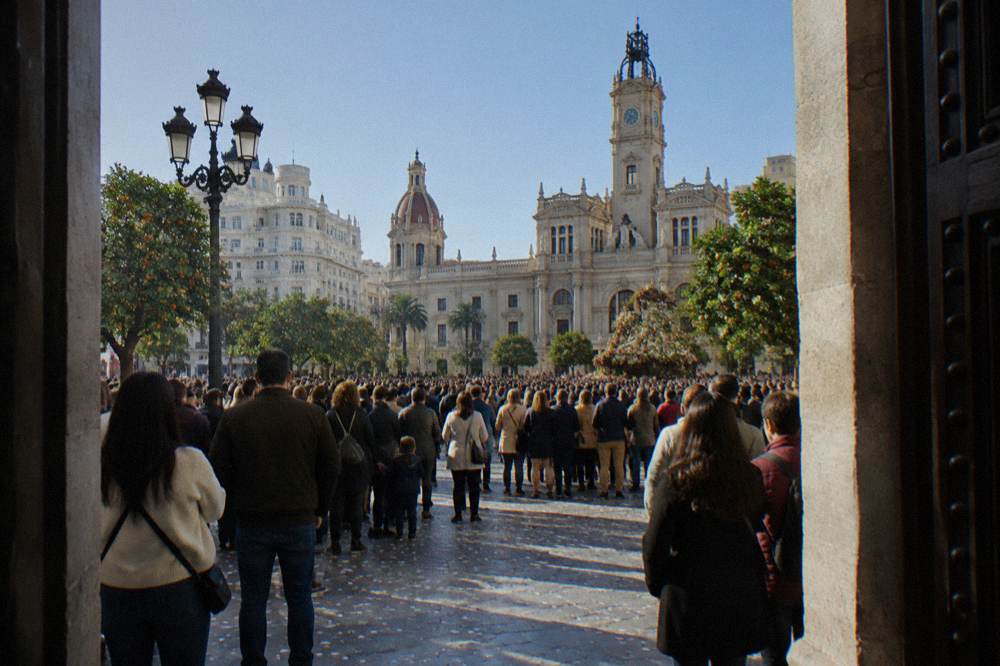 Crowded square with ornate buildings and a wide stone plaza under blue sky