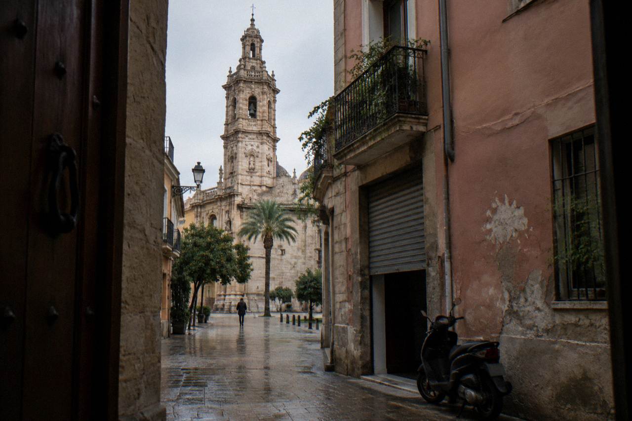 Narrow old town street in Valencia with pastel facades and the bell tower of Santa Catalina rising above the rooftops
