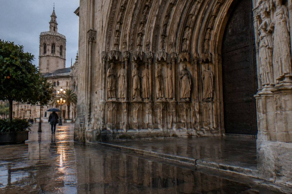 Gothic cathedral doorway with carved stone arches seen from a narrow wet street