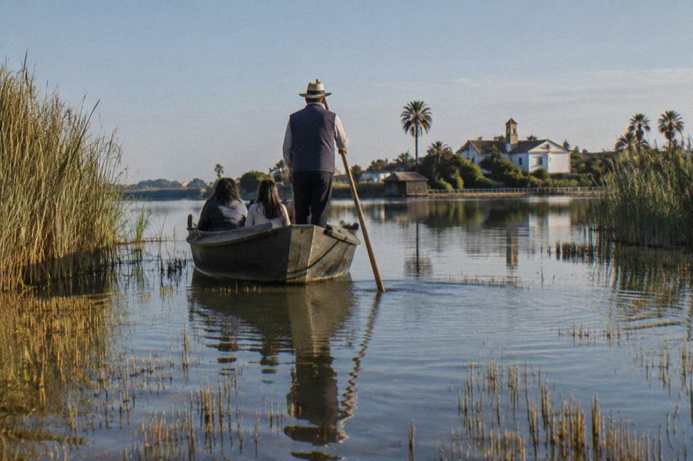 Flat-bottomed boat crossing shallow lagoon water between reed beds