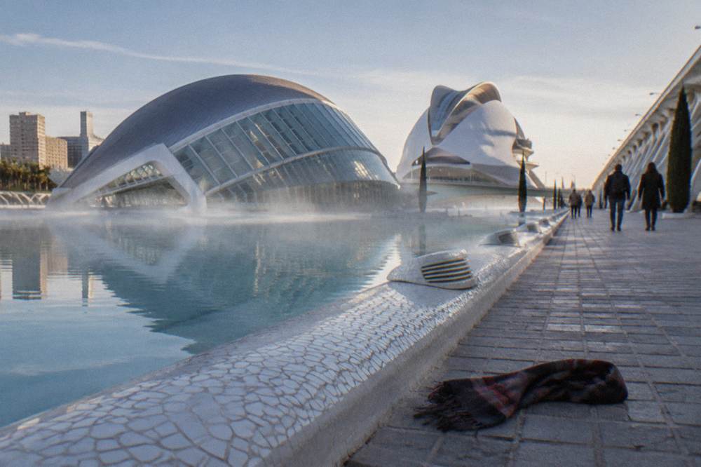 Visitors walking the promenade between the reflecting pools and white buildings