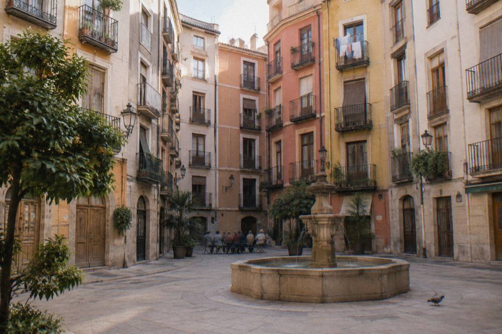 A guide speaking to a small group in a sunlit Valencia square