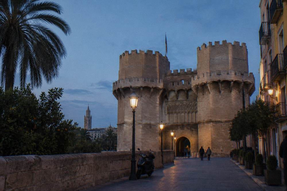 A medieval stone gate tower rising above city rooftops in the evening light