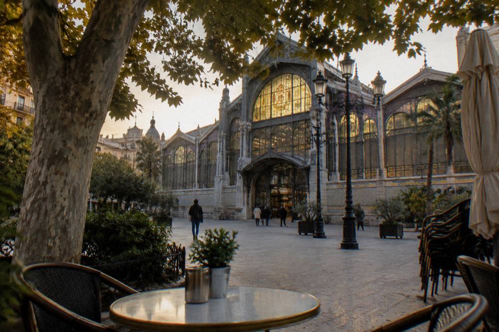 A market hall with a stained glass roof and produce stalls seen from the square outside