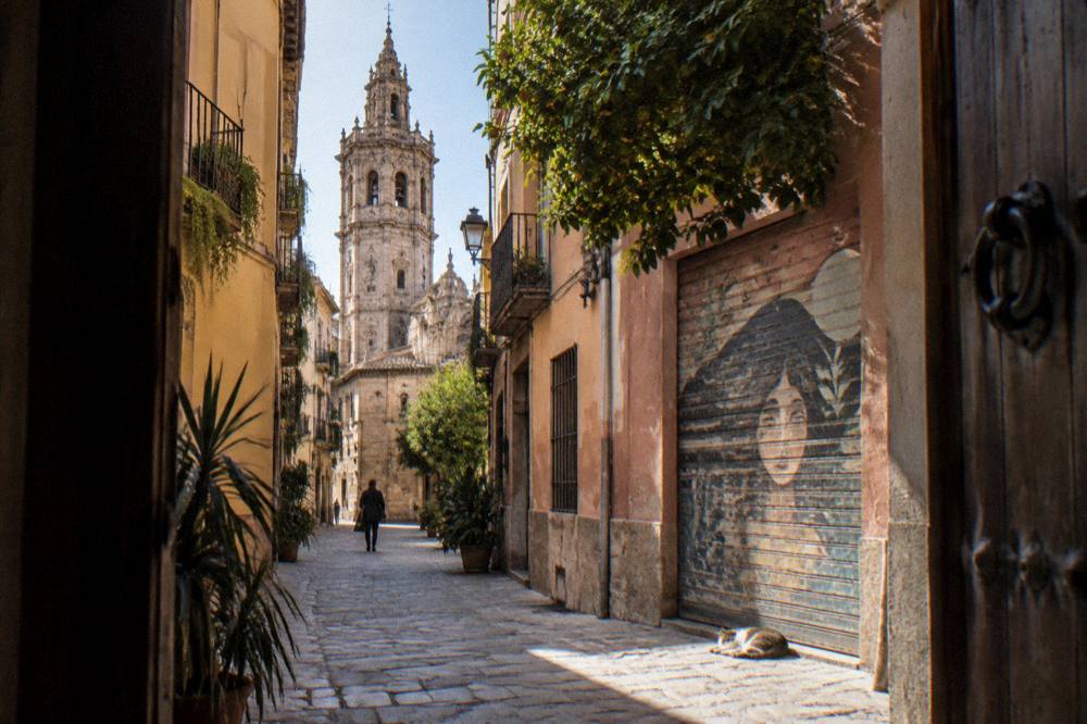 A narrow old town street with pastel facades and stone buildings leading toward a church tower