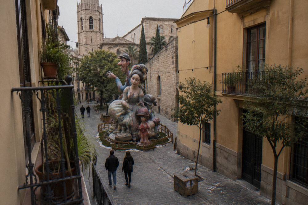A large satirical falla monument with painted figures towering over a narrow Valencia street