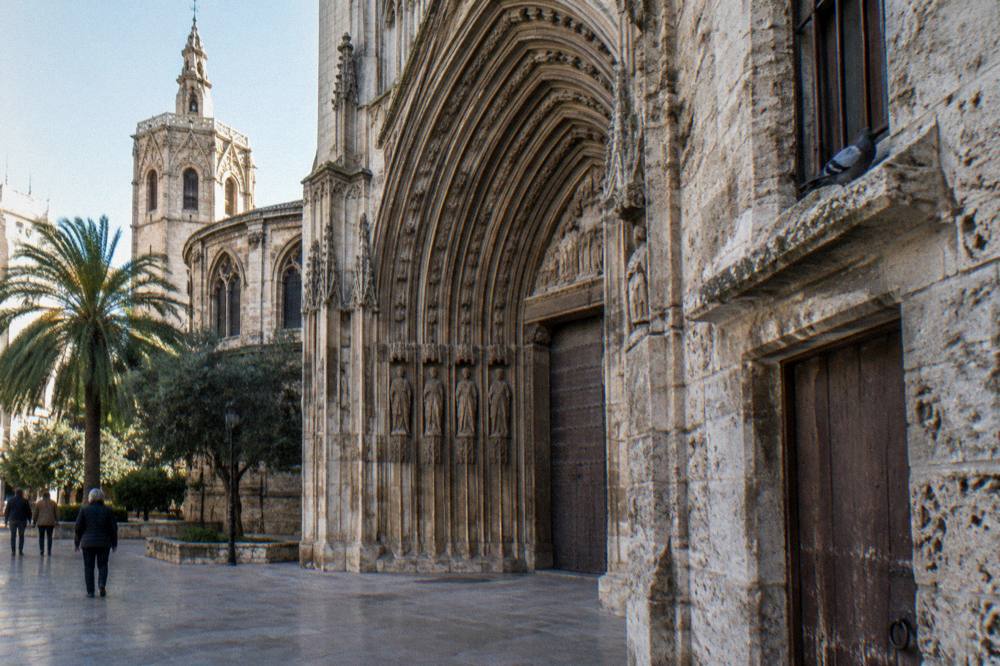 A Gothic stone gateway with arched doorways and weathered walls seen from a city street