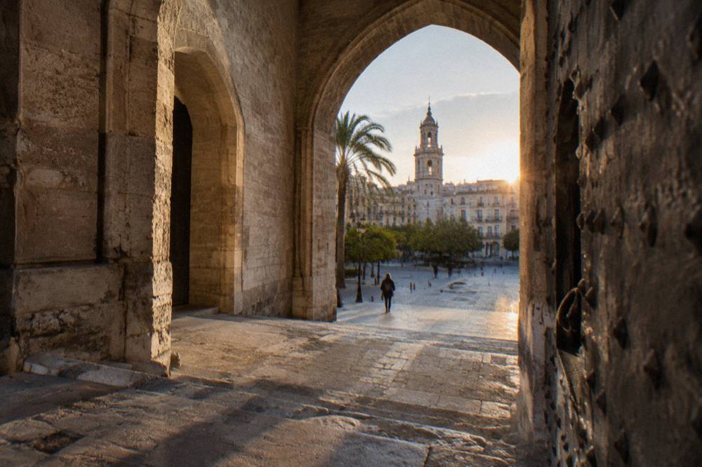 Gothic stone gateway with arched doorways opening onto a cobbled square