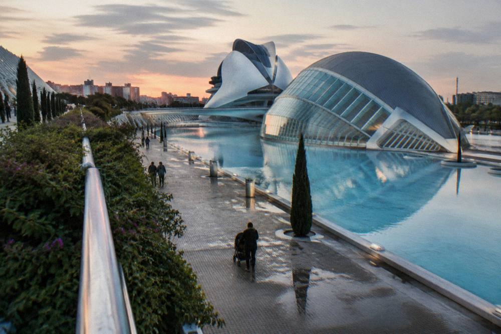Futuristic white buildings reflected in shallow pools along a wide promenade