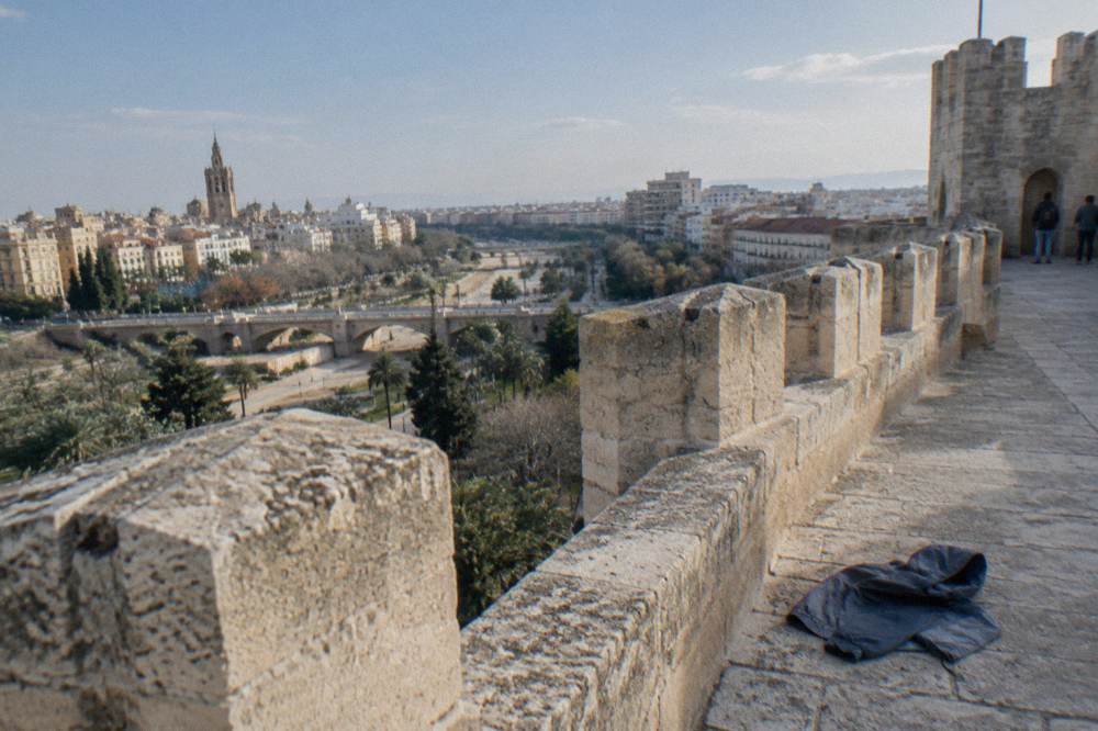 The open upper platform of a stone gate tower with crenellated walls and rooftops beyond