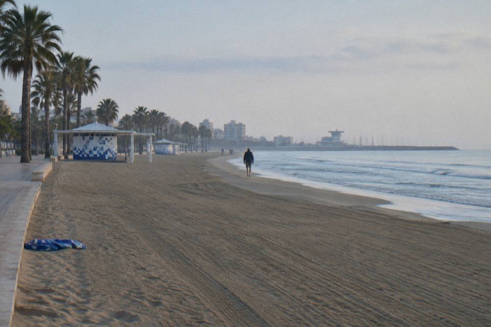 Empty sandy beach in early morning light with gentle waves and distant promenade railings