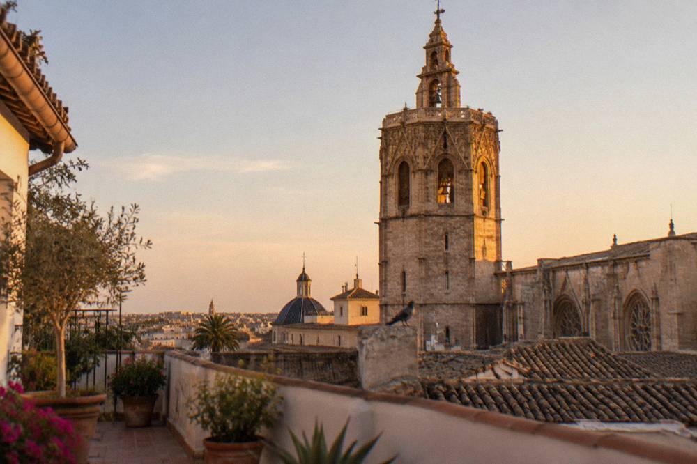 Tall stone bell tower with arched openings rising above rooftops in evening light