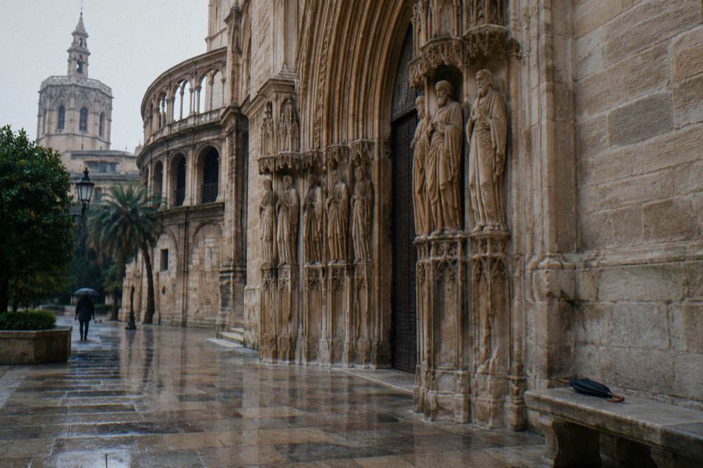 Carved Gothic cathedral side doorway in pale stone on a wet cobbled lane
