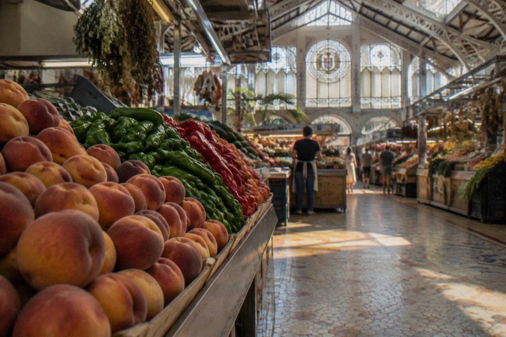 Produce stalls with stacked fruit under the market's iron and glass roof