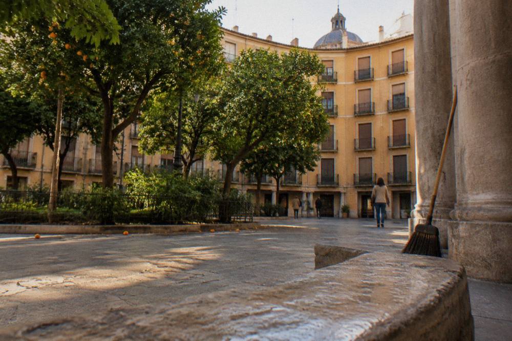 Sunlit old town square in Valencia with orange trees and historic stone buildings