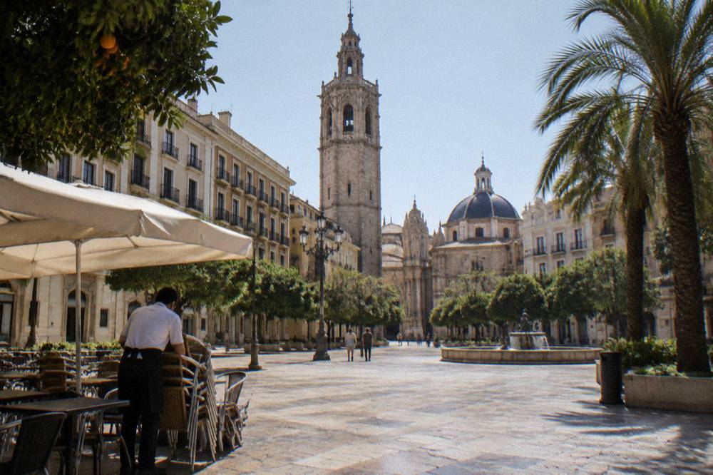 Sunlit plaza with historic facades and a bell tower in the background