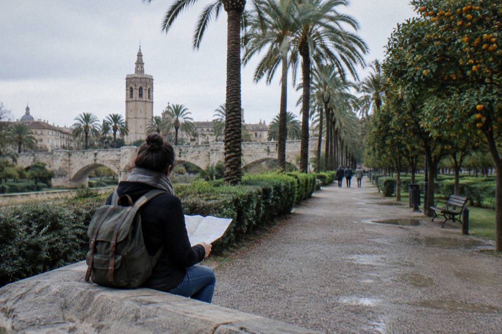 A visitor with a city map resting on a bench beside the Turia gardens